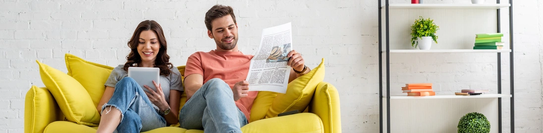Eine Frau und ein Mann sitzen auf einem Sofa und lesen die digitale und gedruckte Tageszeitung